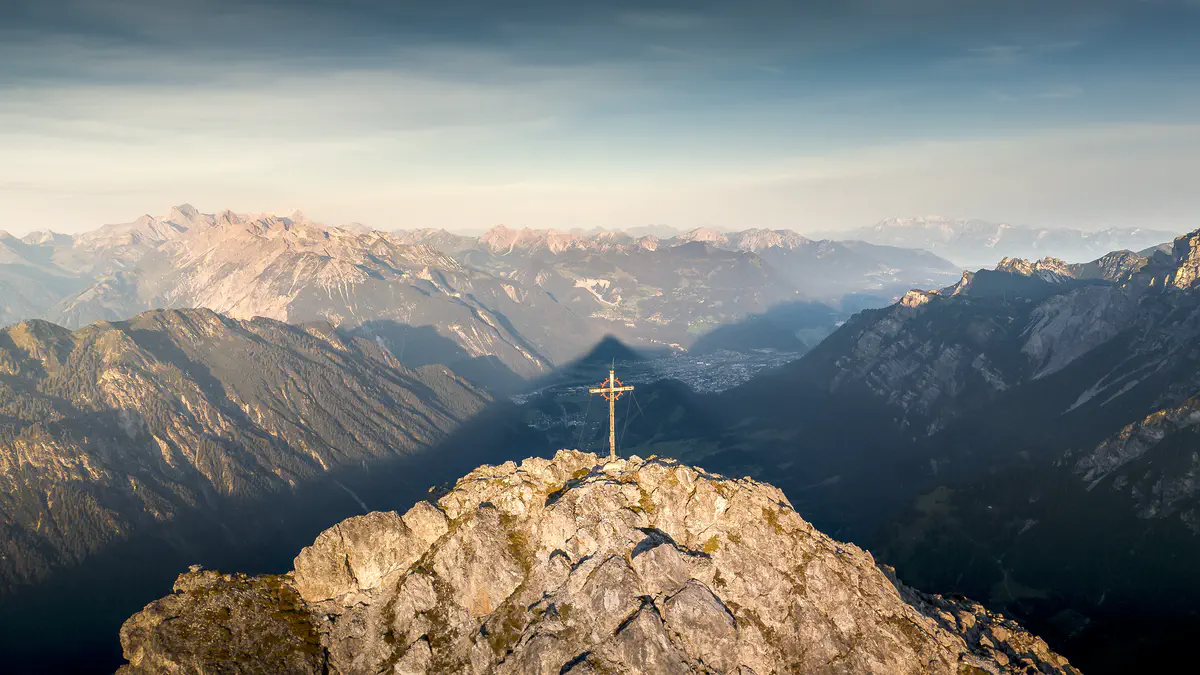 Cross on top of a mountain with great many mountain as background
